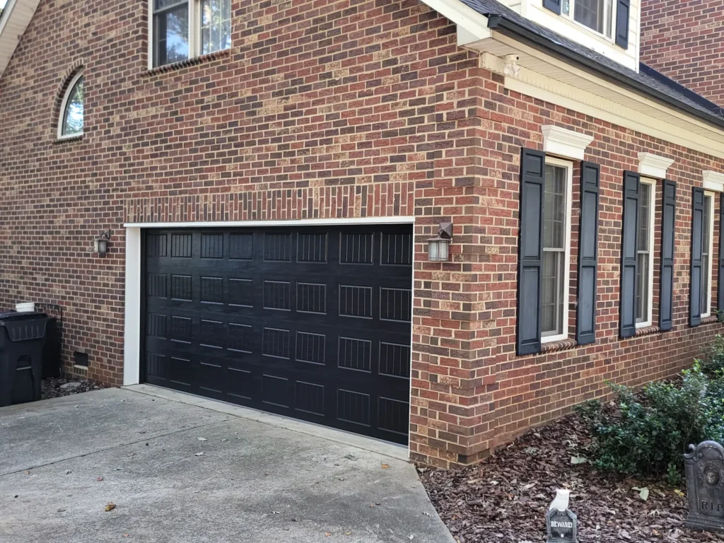 Black raised panel garage door installed on a brick home