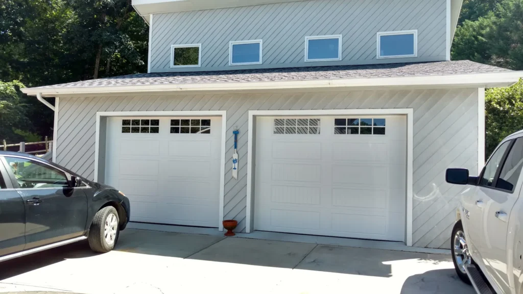 Two white garage doors with windows on a home with light gray siding