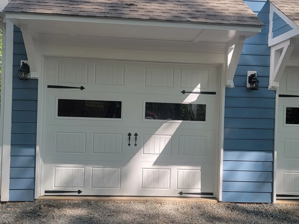 White carriage style garage door with windows and black hardware on a blue sided home